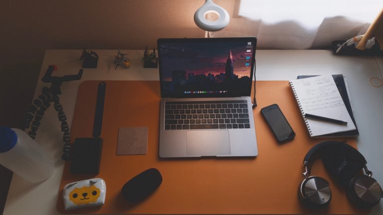 macbook auf tisch neben kopfhörern notizblock und anderem