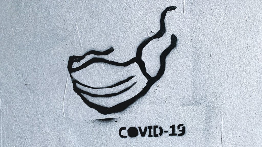 grafitto einer maske mit dem schriftzug covid-19