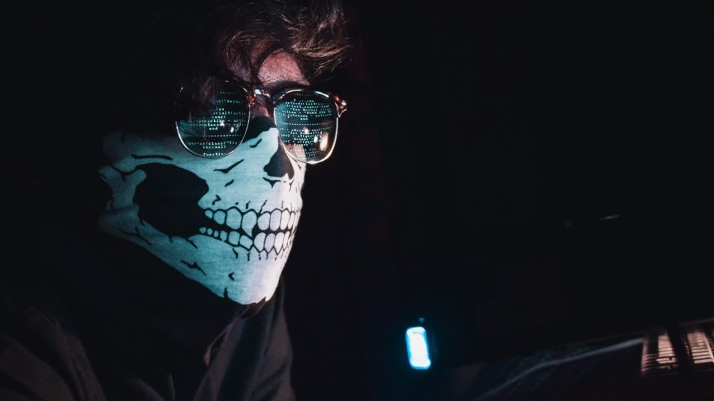 mann mit totenkopfmaske und brille vor monitor