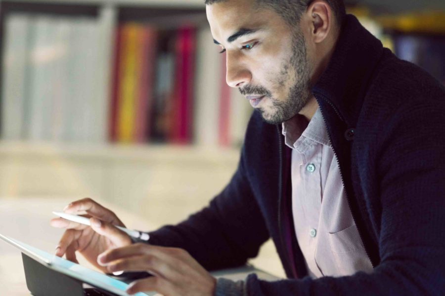 Shot of a focused young man working on a digital tablet in his home office in the early evening.